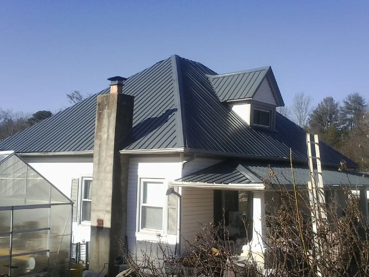 Dark blue standing seam metal roof on a white farmhouse with dormer — Slate & Tile Roof Repair by Roofing Brothers in Lynnville