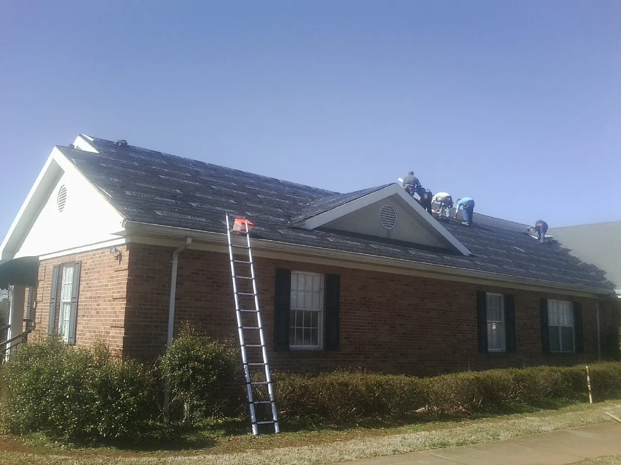 Crew tearing shingles off a brick ranch roof with a ladder set — Metal Roof Repair work by our crew in Lynnville