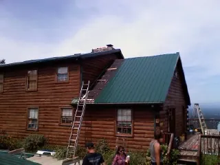 Green metal roof going on a two story log home with ladders set in Lynnville